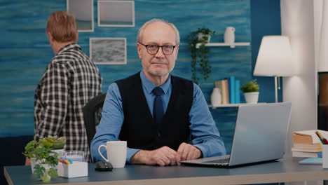Elderly businessman entrepreneur sitting in workspace looking at camera