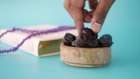 close-up of dates in a wooden bowl with a quran and prayer beads