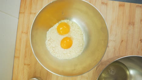 rompiendo dos huevos en harina en un tazón para mezclar, haciendo y horneando mezcla para pasteles en casa