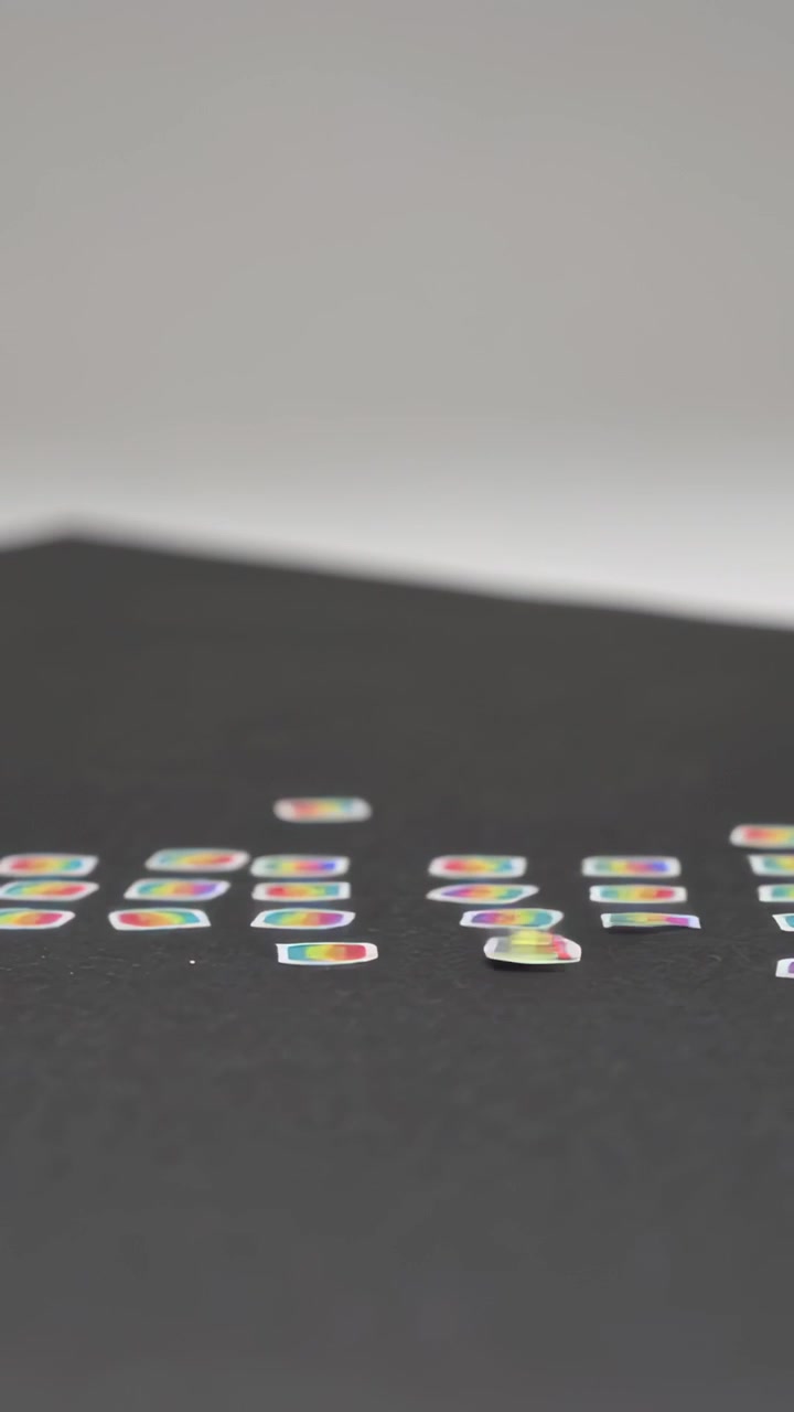 Vertical video: Dropping from above rainbow pieces scattering and settling into grid on black table