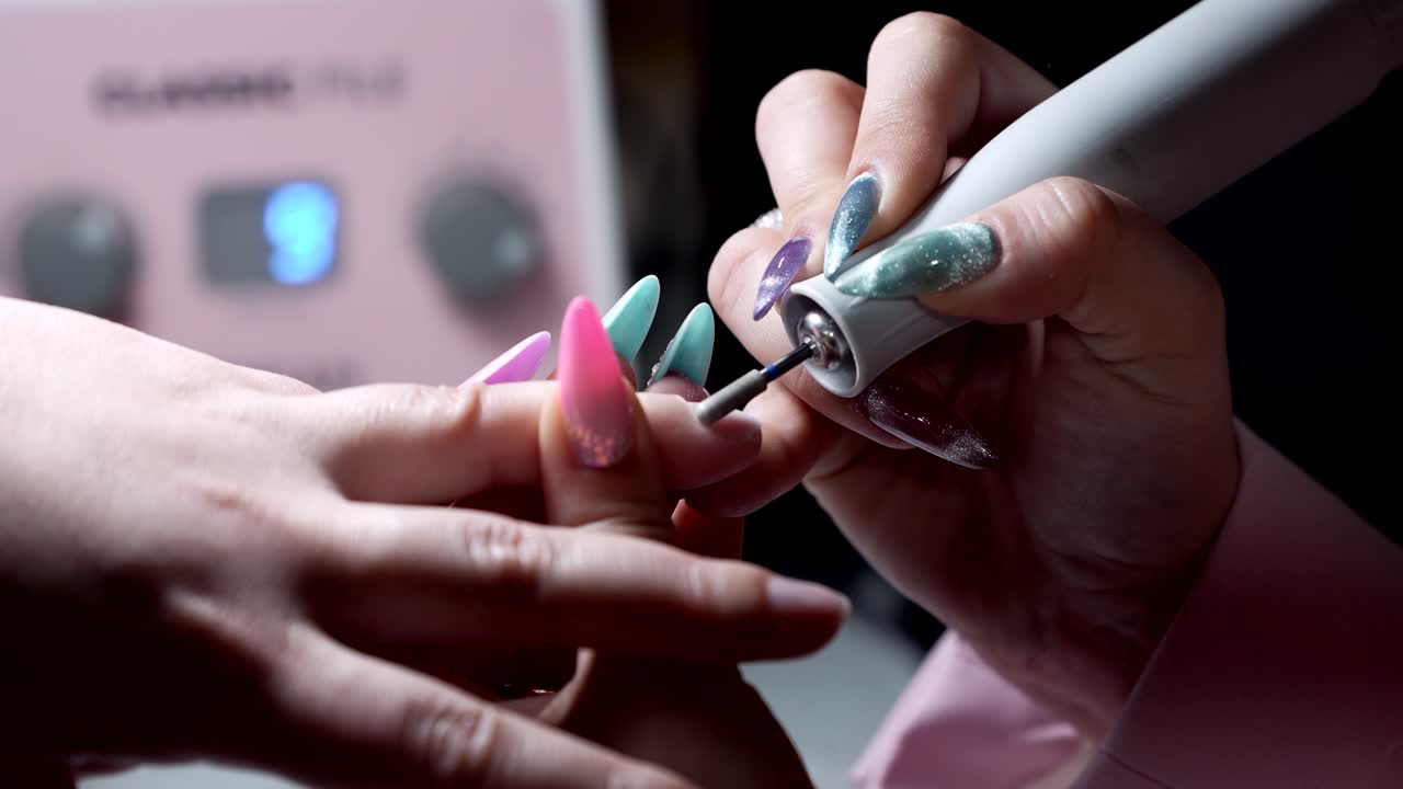 Nail technician using electric drill to shape pink acrylic nails in salon
