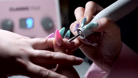 nail technician using electric drill to shape pink acrylic nails in salon