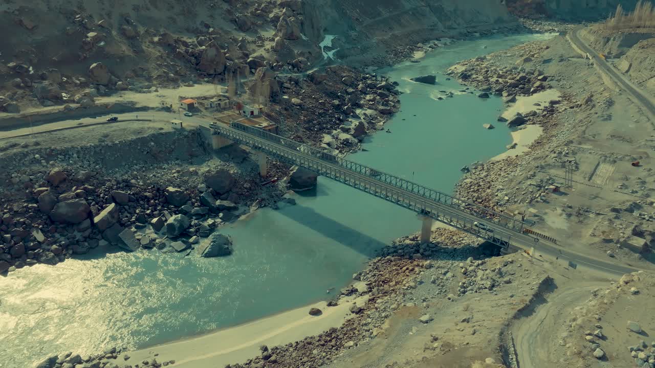 Cars drive across a bridge that passes a river in Skardu - drone flies slowly towards the sky