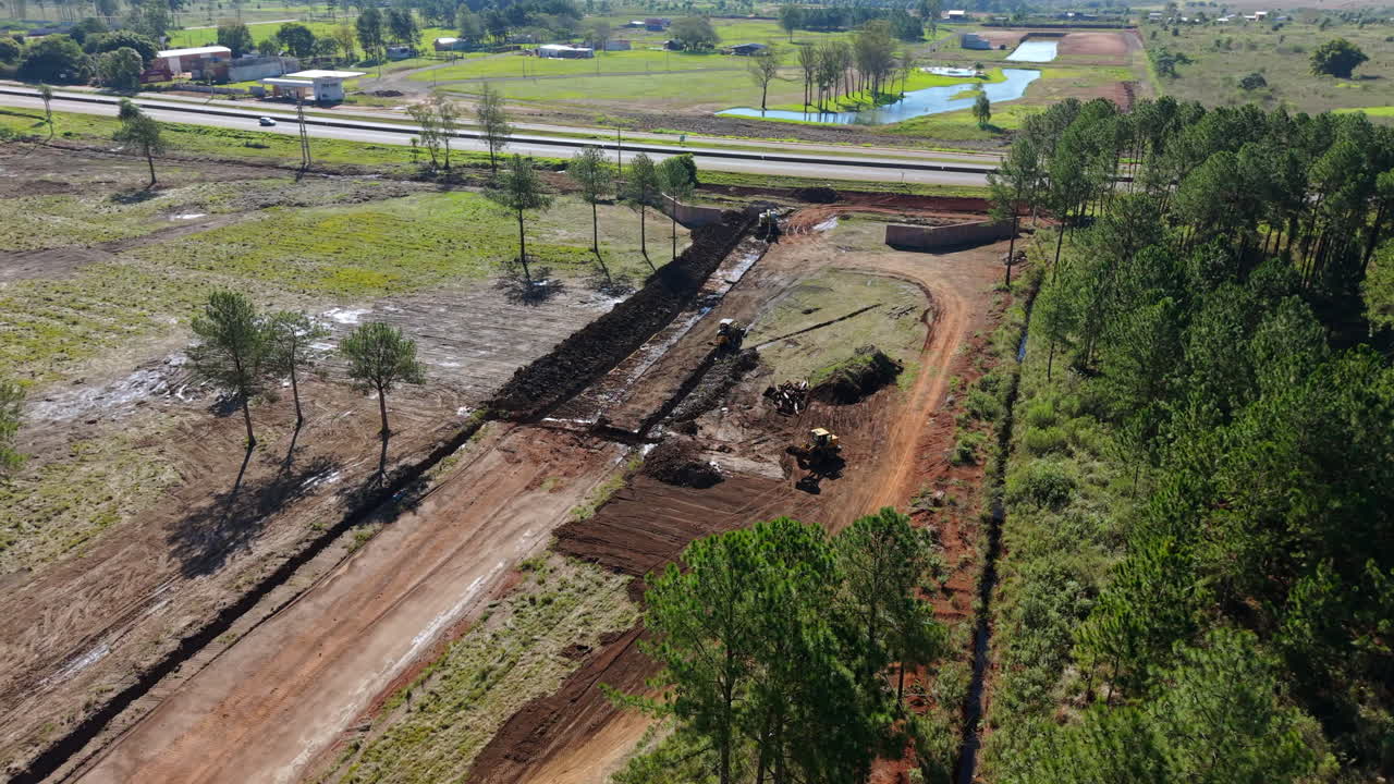 Road construction site with machinery and trees around, aerial view