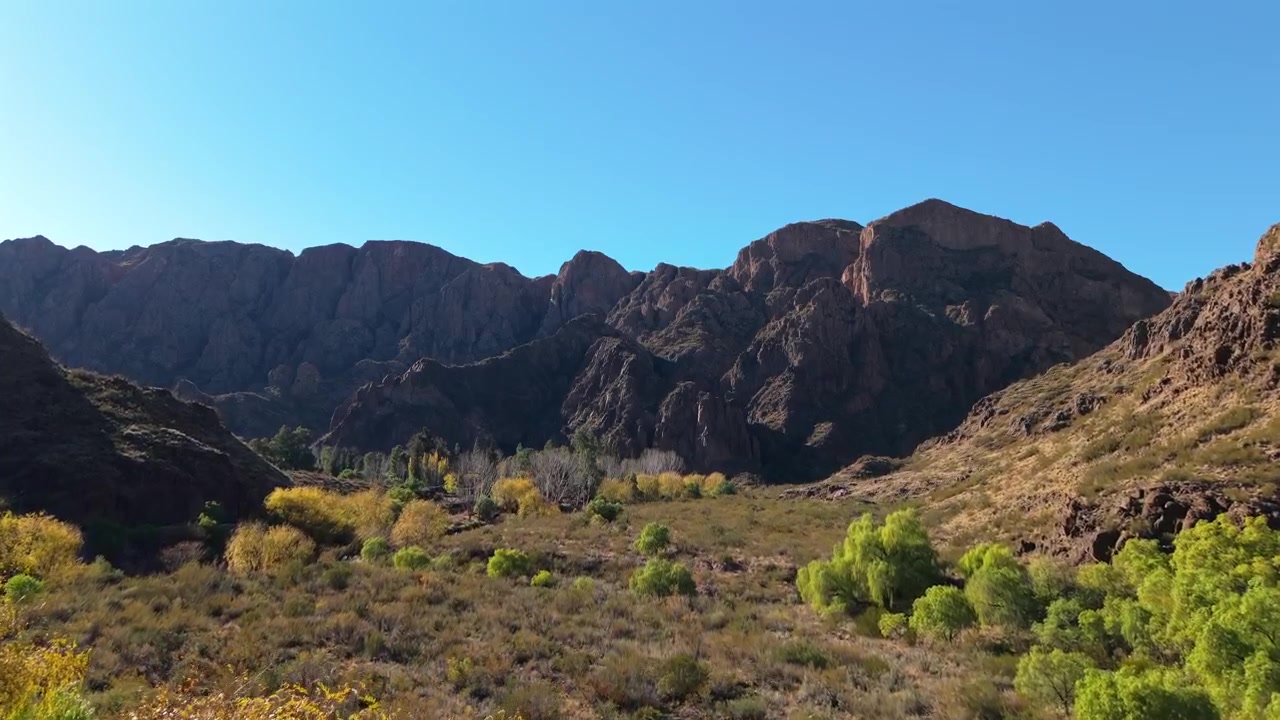 Strada Provinciale 173, che mostra una valle montuosa rocciosa e aspra con alberi dai colori autunnali e vegetazione arida. Ascesa aerea in avanti in una mattina soleggiata e con cielo azzurro