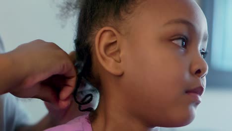cerca de una niña afroamericana trenzando su cabello en casa durante la ordenanza de quedarse en casa