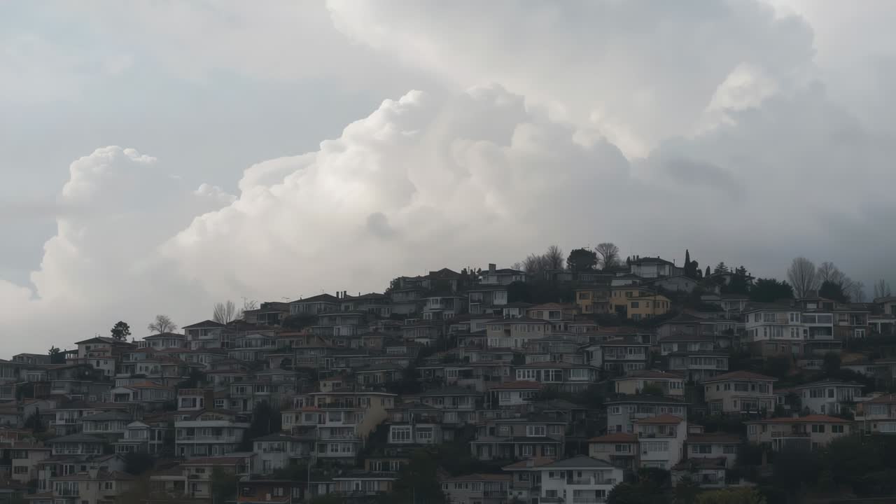 Nuvole spinte dal vento, che si muovono sopra una fitta collina, alterando la luce su tetti e camini.