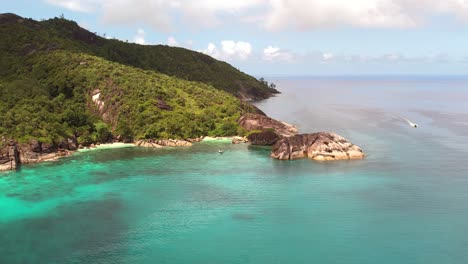 Drohnenaufnahme-Eines-Vorbeifahrenden-Bootes,-üppiger-Berg-Mit-Riesigem-Granitstein,-Mahe,-Seychellen-60-Fps