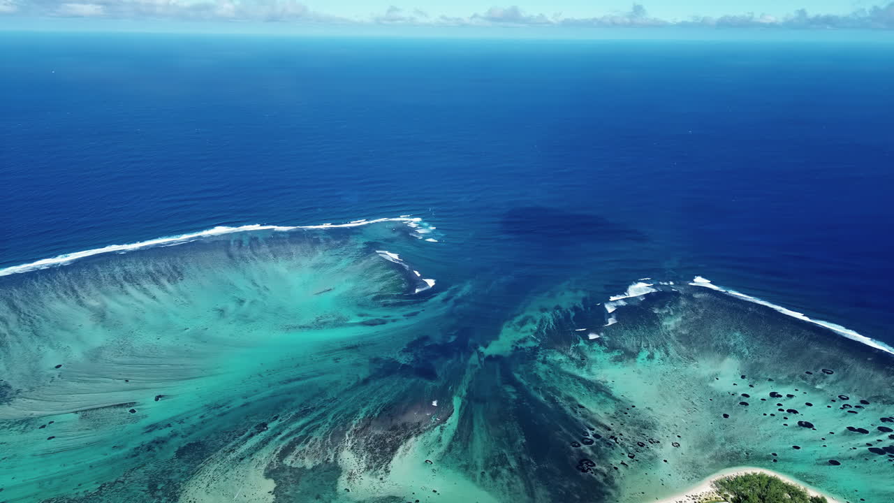 Vue aérienne par drone des eaux turquoise du lagon et des formations de récifs coralliens à l'île Maurice, avec des vagues se brisant le long de la ligne du récif dans l'océan Indien.