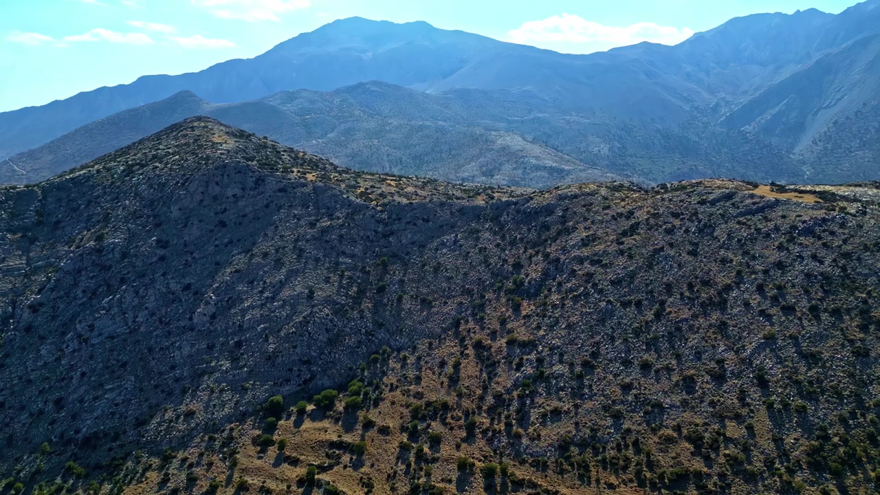 Crinali rocciosi e scarsamente vegetati a Katafigio Agrias Zois Trigiodo sono filmati dall'alto con cime montuose stratificate in lontananza.