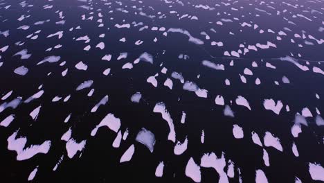 vista aérea de arriba hacia abajo del hielo oscuro de un lago congelado con pequeñas islas de nieve al amanecer