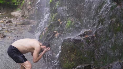 strong man getting wet under waterfall. slow motion.