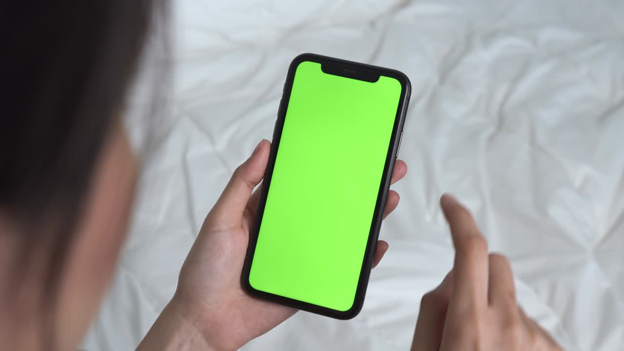 Donna che tiene un mockup di smartphone con schermo verde e un messaggio digitato sul letto a casa