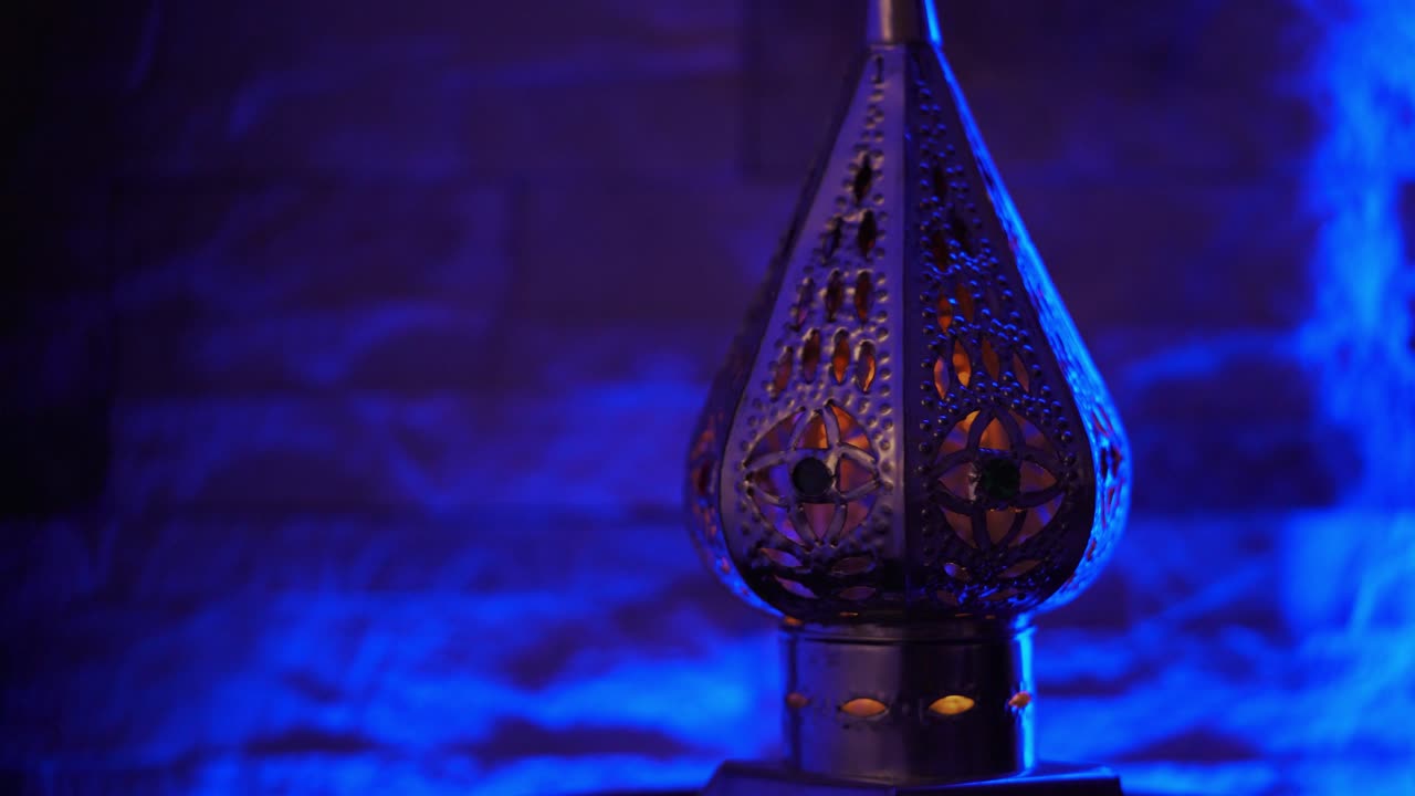 lámpara de estilo marroquí oriental con velas encendidas girando sobre un fondo azul vibrante