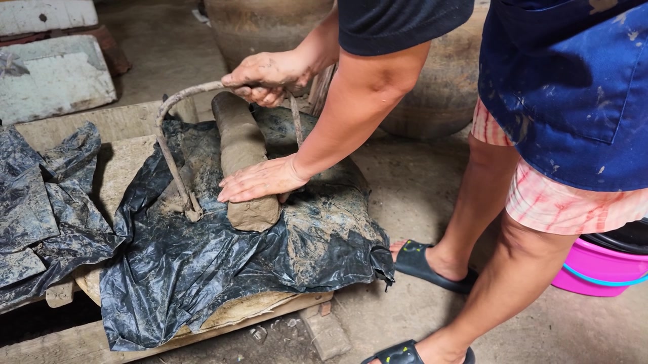 Artisan uses wire tool to slice raw clay in a pottery workshop on Koh Kret.