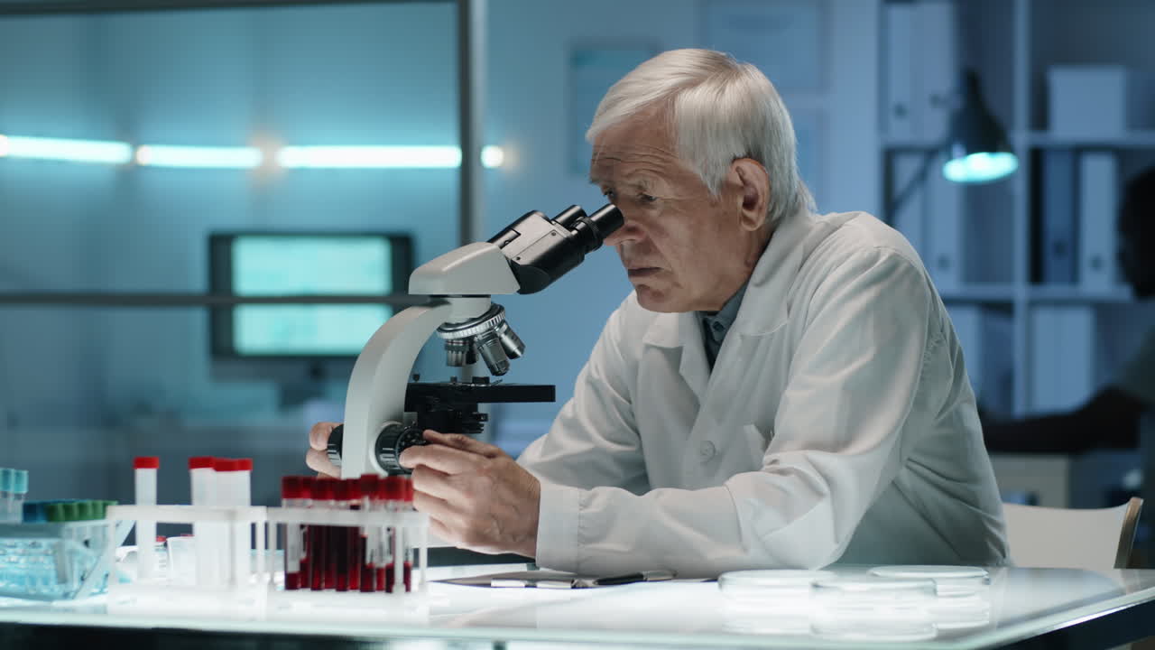 científico sénior trabajando con el microscopio y tomando notas