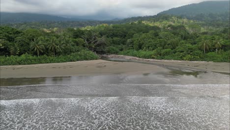 Wellen-Krachen-Am-Strand-Von-Costa-Rica,-Während-Sie-In-Die-Leuchtend-Grüne-Vegetation-Fliegen