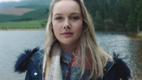 retrato hermosa mujer rubia sonriendo sintiéndose feliz disfrutando del frío invierno al aire libre junto al lago con el viento soplando el pelo 4k