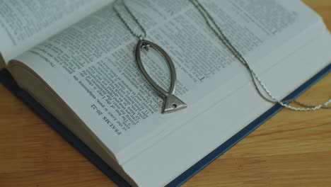 close-up of opened bible book with psalms text and ichthus necklace