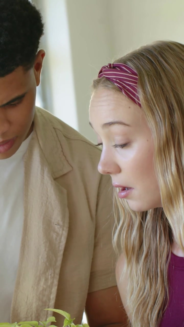 Vertical video: Seeing seedling, couple leaning in at home, checking plant, woman in maroon top