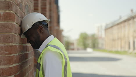 stressed construction worker leaning on brick wall