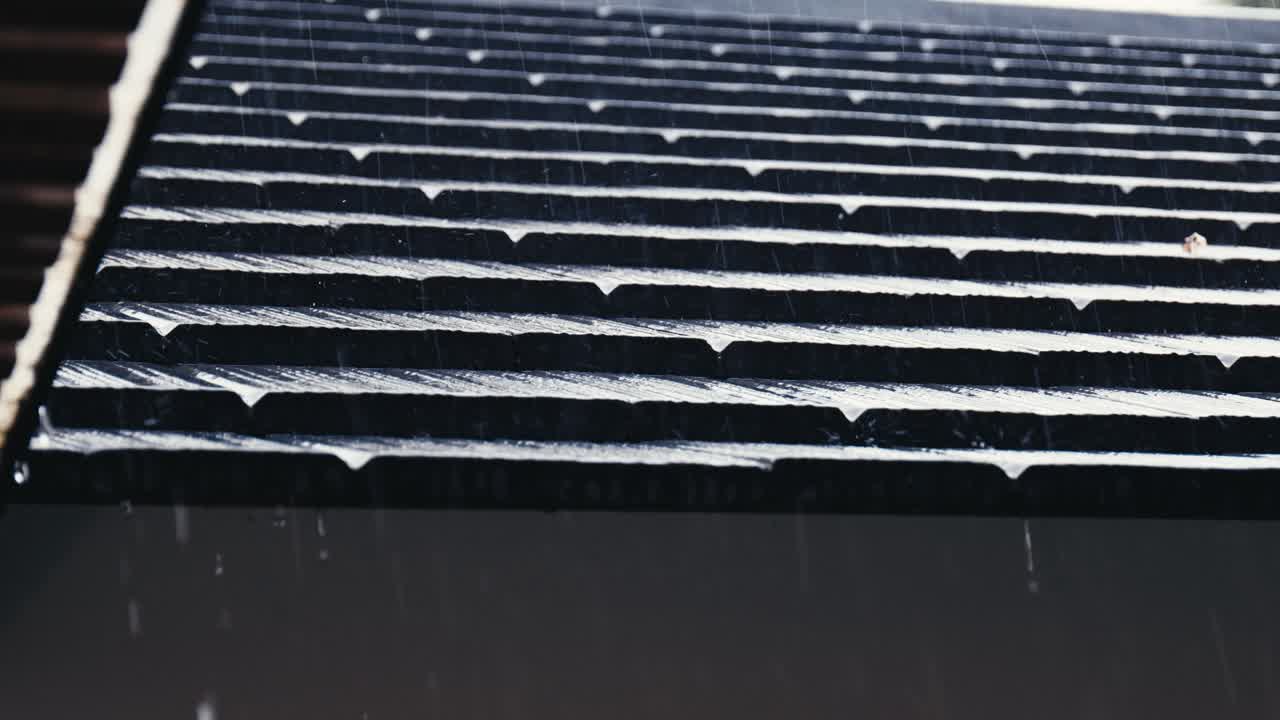 Rain is trickling down from the eaves and roof tiles of a house