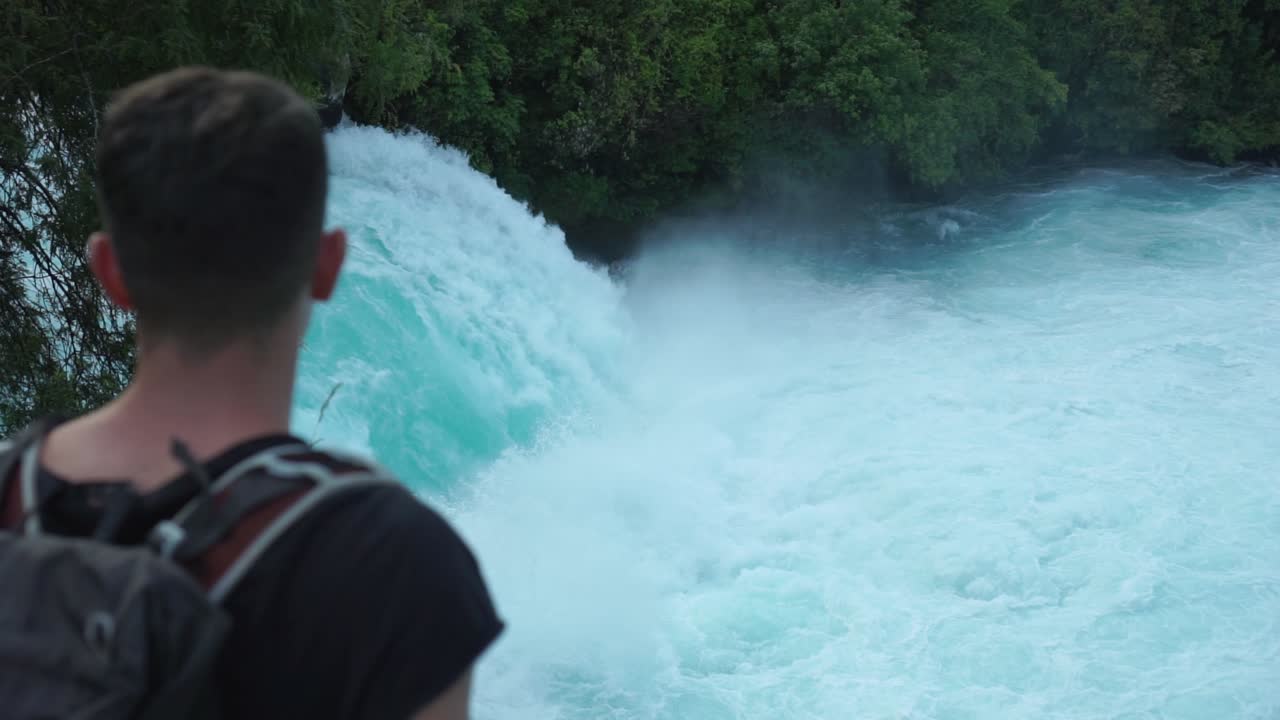slowmo - joven turista caucásico desde atrás mira las cataratas huka, nueva zelanda