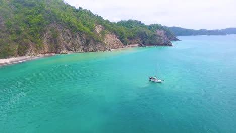 drone shot of a yacht anchored offshore from a deserted tropical island in central america in an ocean of turquoise blue water
