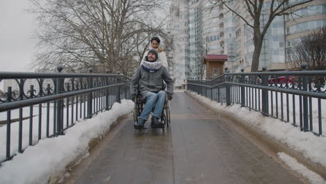 front view of a muslim woman taking her disabled friend in wheelchair on a walk in city in winter 1