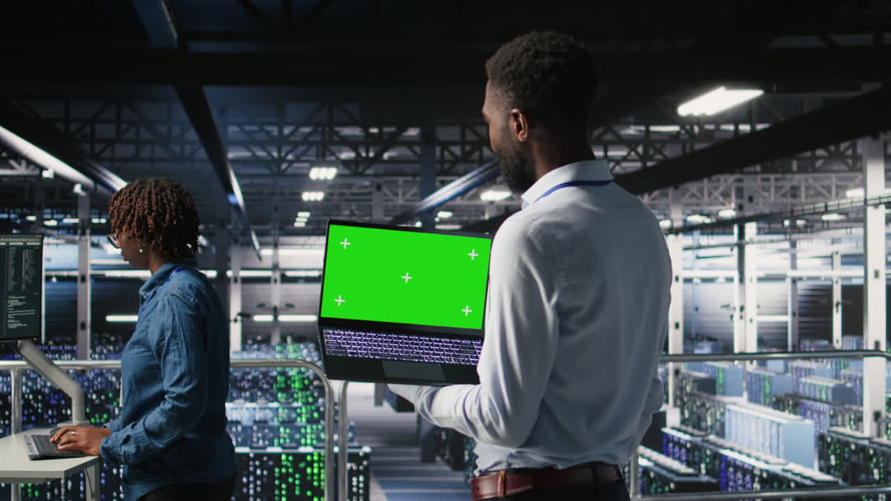 Technicians in data center analyzing performance outputs on green screen laptop
