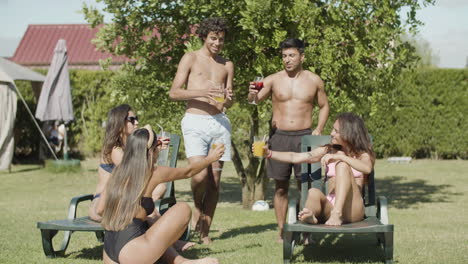 cute men and women in swimsuits clinking glasses on backyard