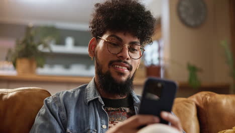 hombre sonriendo y mirando su teléfono mientras está sentado en un sofá
