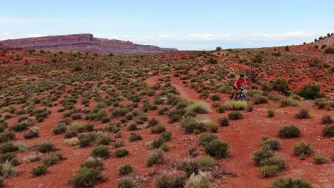 aerial dolly backward shot of mountain biker towards camera in red moab desert