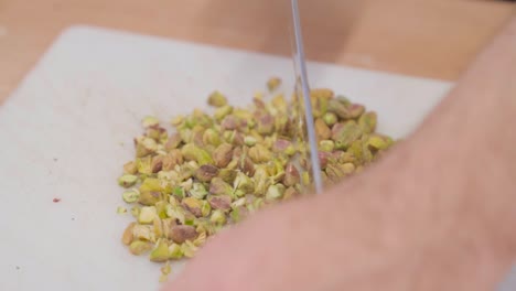 Close-up-of-hands-chopping-pistachios-on-a-cutting-board-in-slow-motion,-kitchen-setting