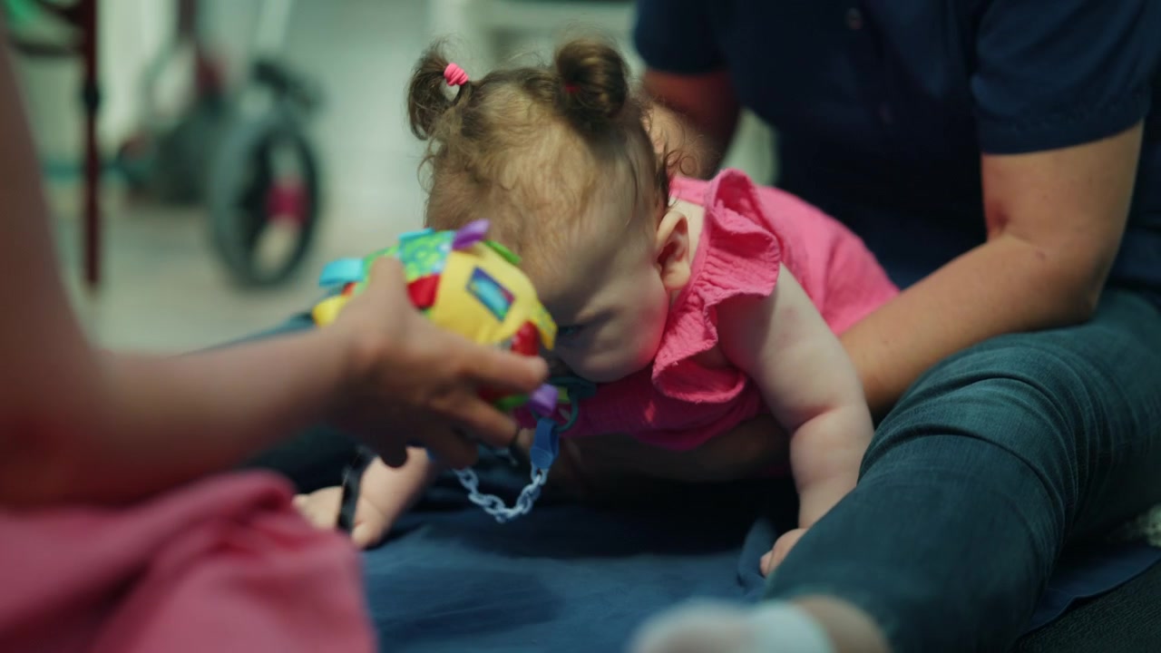 Baby girl with medical condition performing physical exercises on floor with therapist. Focusing on development and mobility
