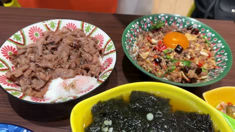 a vibrant overhead sequence of assorted asian rice bowls with beef, shrimp, egg, vegetables, and seaweed soup, under bright indoor lighting with smooth camera panning