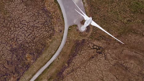 drone shot flying over a wind turbine in operation by a single track road