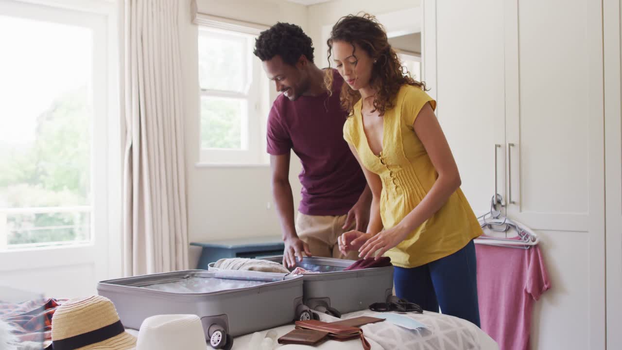 Happy biracial couple packing clothes into suitcase together, preparing for travel