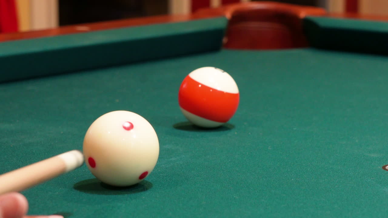 Closeup of Person Playing Pool Shooting Striped Orange 13 Ball into Corner Pocket after Practice Strokes using Cue Ball with Red Spots, Open Bridge Hand with Wooden Cue Stick and Green Felt or Cloth