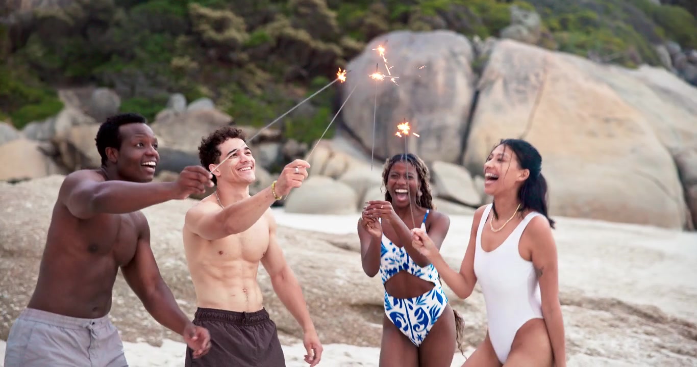 Gruppo di amici con stelle filanti scintillanti su una spiaggia al tramonto