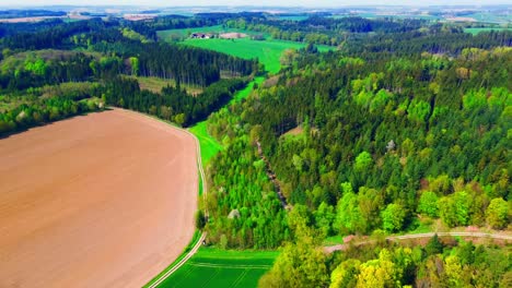 vista aérea de un campo arado adyacente a un denso bosque y tierras de cultivo verdes