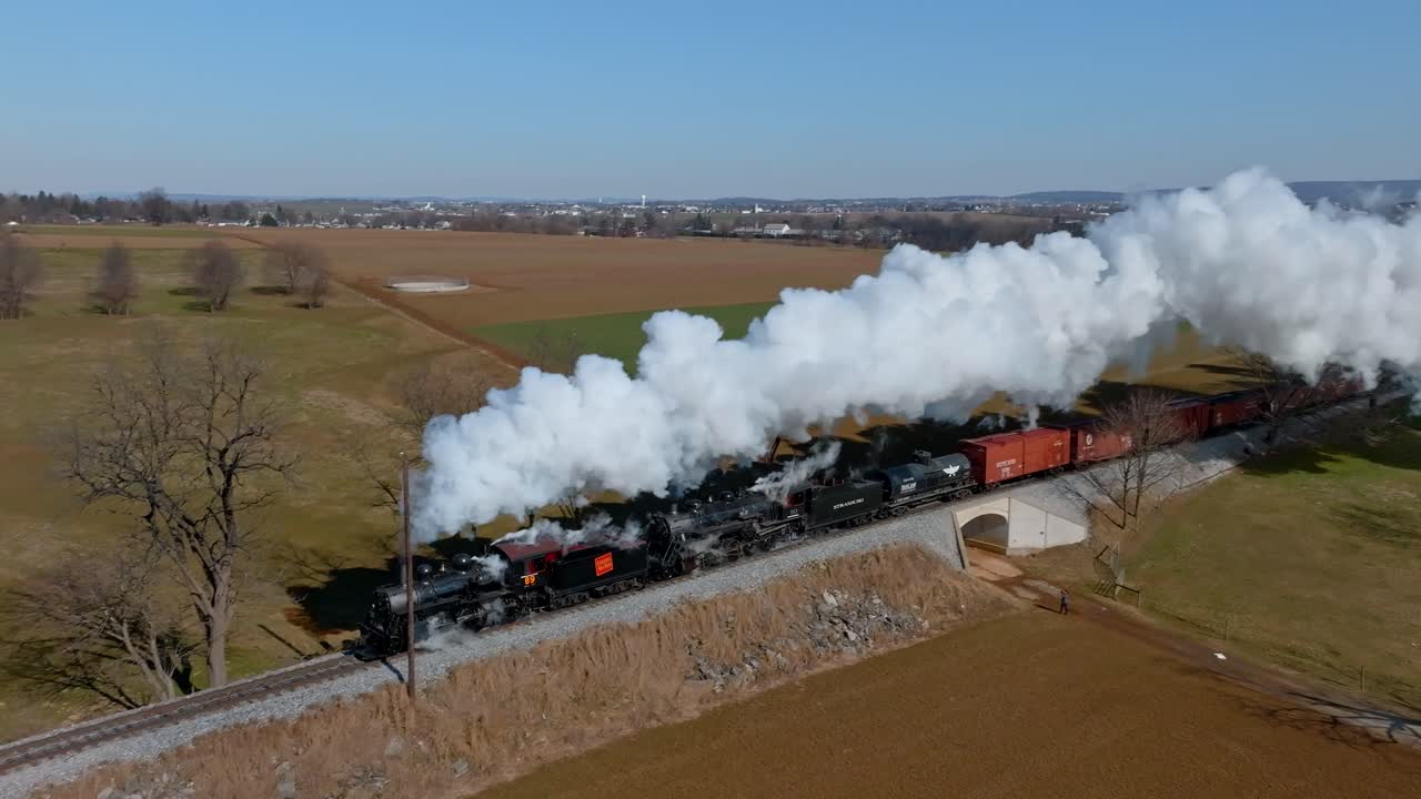 Classic double header steam locomotive chugs along scenic tracks, billowing clouds of steam into the sky passing through vibrant green fields in Pennsylvania