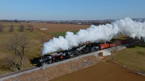 classic double header steam locomotive chugs along scenic tracks, billowing clouds of steam into the sky passing through vibrant green fields in pennsylvania