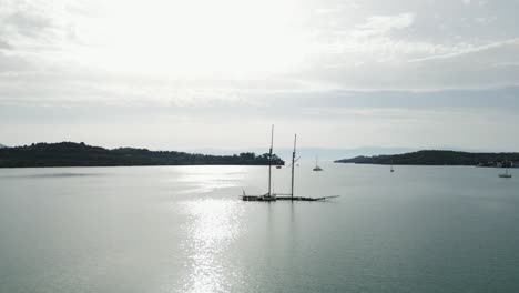 Shipwreck-in-silver-shimmering-sea-water,-aerial-panorama-of-sunlit-peaceful-bay