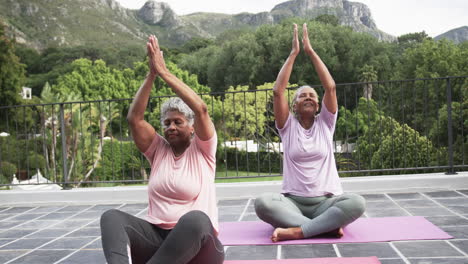 senior african american female friends practicing yoga meditation sitting on balcony, slow motion