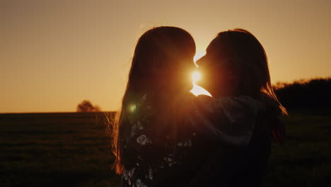 una mujer besa tiernamente a su hija el sol al atardecer ilumina bellamente sus siluetas 4k