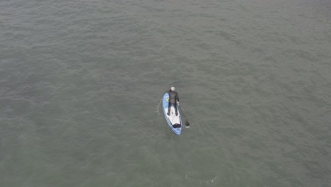 antena de alto ángulo del hombre de traje de neopreno en stand up paddleboard, agua entrecortada