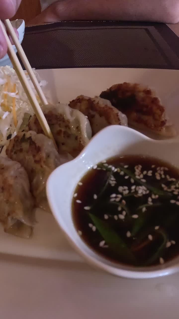 Dumplings or gyoza being dipped into soy sauce with sesame seeds using chopsticks, close up