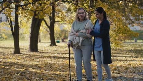 Young-female-nurse-helping-senior-woman-walking-in-park