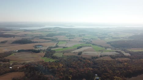 aerial view over rolling farmland and patchy fields with lake wisconsin shimmering in the distance. captures rural midwest landscape under clear morning light.